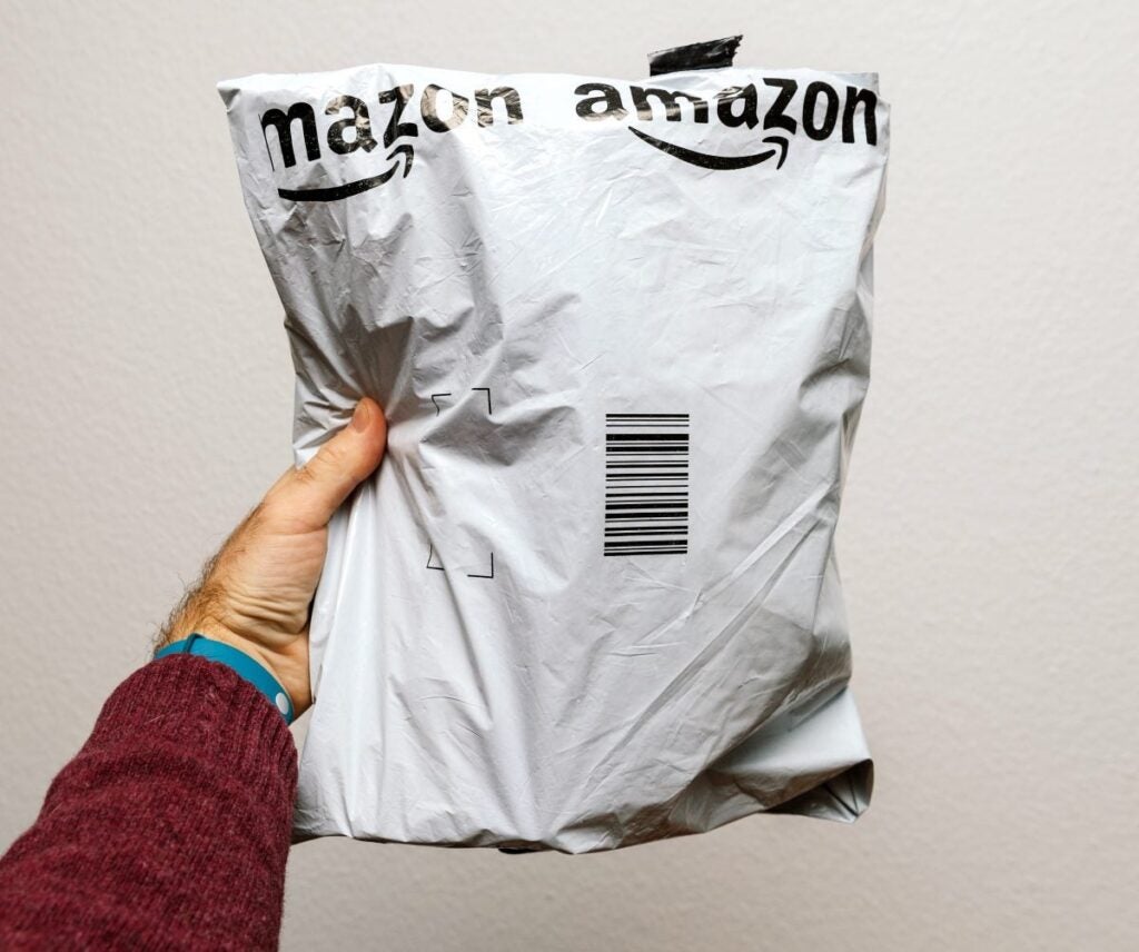 <i>Photo Credit: Shutterstock/Hadrian</i> A person holding an Amazon plastic bag